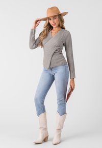 Maglione grigio a coste avvolgente, jeans skinny blu chiaro, stivali da cowboy beige con tomaia testurizzata e cappello di paglia beige a larga tesa.