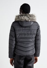 Giacca puffa grigia scura con design a righe orizzontali, cappuccio e rifinitura in pelliccia sintetica. Texture liscia con un aspetto leggero e isolato.