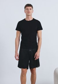 Μαύρο κοντομάνικο μπλουζάκι σε συνδυασμό με χαλαρά μαύρα σορτς. Το ύφασμα είναι λείο, με απλή γραμμή και χωρίς επιπλέον σχέδια ή διακοσμητικά στοιχεία.