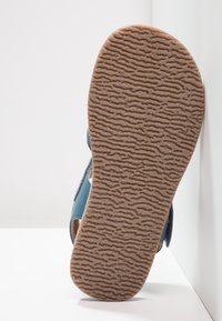 Modré kožené sandály s texturovanou hnědou gumovou podrážkou s vlnkovým vzorem. Otevřený design s bočními výřezy pro ventilaci.