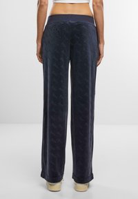 Navy velour sweatpants with a flat waist, loose fit, tonal "Juicy" logo pattern, and cuffed hems. Smooth texture and relaxed silhouette.