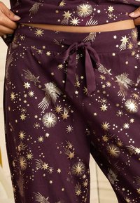Conjunto de pijama púrpura con cintura ajustable, que presenta patrones de estrellas y cometas doradas a lo largo de la tela, creando un diseño festivo.