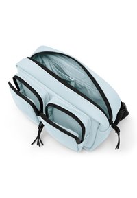 Ljust blått vadderat väska med en dragkedja på toppen, som har två framfickor med svarta dragkedjor. Slät textur och rundade hörn.