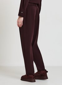 Pantaloni bordeaux dalla vestibilità comoda, dotati di cintura, tasche e una texture liscia, abbinati a stivali in suede marrone con suola chunky.
