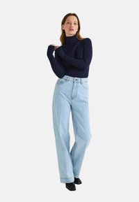 Pull col roulé côtelé bleu marine associé à un jean large taille haute bleu clair. Des bottines noires à bout pointu complètent le look.