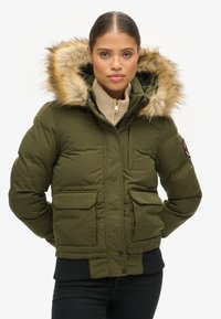 Groene pufferjack met een met bont gevoerde capuchon, geribbelde manchetten en twee voorzakken. Voorzien van een ritssluiting en een logo-patch op de mouw.