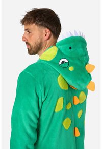 Un morbido e verde felpato intero con un design di dinosauro, dotato di cappuccio, accenti gialli e arancioni, e dettagli a forma di spine lungo la schiena e il cappuccio. Texture soffice.