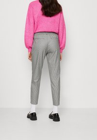 Pantalons à carreaux gris et blancs avec une coupe ajustée, dotés d'une taille, de poches latérales, associés à des chaussures noires et des chaussettes blanches.