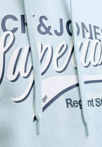 Sweat à capuche bleu clair à texture douce ; présente un texte imprimé graphique en bleu foncé et blanc, des cordons de serrage réglables et une coupe décontractée.
