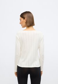 Μακρυμάνικο, ελαφρύ τοπ σε κρεμ χρώμα με κάθετες ρίγες και υφή. Στρογγυλή λαιμόκοψη και άνετη εφαρμογή.