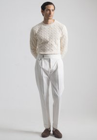 Suéter de punto grueso color crema combinado con pantalones blancos de cintura alta con botones laterales. Mocasines marrones completan el conjunto.