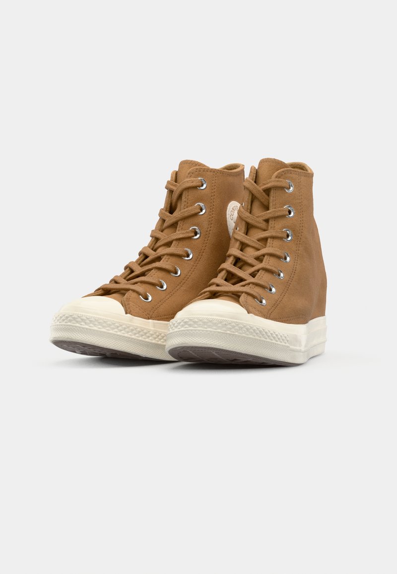 Sneakers alto marroni in suede, con suole in gomma bianca, occhielli metallici e un patch logo circolare sul lato esterno.