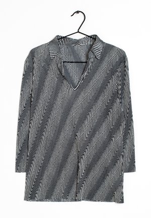 Maglietta a maniche lunghe bianco e nero con colletto, caratterizzata da strisce diagonali di diversi motivi a pois e un design a scollo a V.