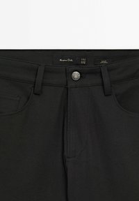 Zwarte slim-fit broeken hebben een gladde textuur, een knoopsluiting en subtiele stikdetails. Label zichtbaar op de tailleband voor merkidentificatie.