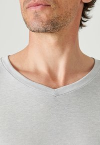 Maglietta grigia chiaro a V in morbido e liscio tessuto. Caratterizzata da un design semplice con maniche corte e una vestibilità comoda, senza pattern o dettagli.