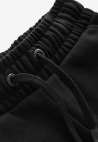 Svarta joggingshorts i mjukt tyg, med ett elastiskt midjeband med veckad textur och justerbar dragsko med plastspetsar.