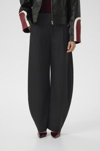 Woman wearing black wide-leg pants, black leather jacket with red and white sleeve patches, and dark red pointed shoes.