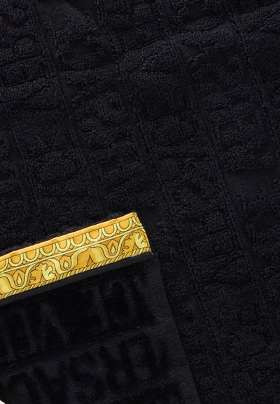 Tissu noir texturé avec motif de texte en relief et bord plié orné d'une bordure ornementale décorative jaune et dorée.