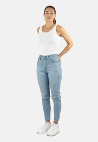 Hellblaue High-Waisted-Jeans mit geradem Schnitt, kombiniert mit einem enganliegenden weißen Tanktop und weißen Sportschuhen. Einfaches Design, ohne Verzierungen.