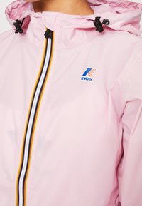 Lyserød vandtæt jakke med en frontlynlås og flerfarvede striber. Inkluderer hætte med snøre og et lille logo.