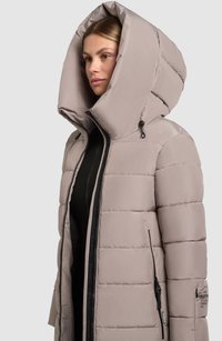 Svetlo béžová prešívaná bunda má veľkú kapucňu, predný zips, bočné vrecká so zipsami a výraznú horizontálne prešívanú textúru.