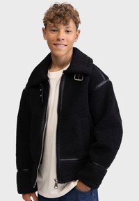 Schwarze Fleecejacke mit durchgehendem Reißverschluss, übergroßem Kragen, Lederakzenten und strukturiertem Finish. Verfügt über Druckknöpfe an der Schulter.