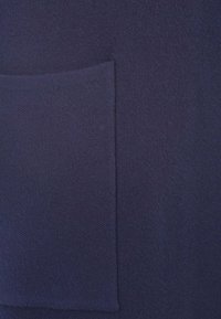 Tessuto di colore blu navy con una tasca a toppa quadrata; presenta un aspetto morbido e lavorato a maglia, evidenziando sottili variazioni di tonalità.
