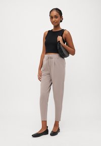 Zwarte cropped tanktop, beige tapered broek met trekkoord, zwarte flats en een kleine zwarte handtas met geperforeerde details.