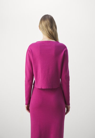 Fuchsia Strickpullover mit langen Ärmeln und cropped Design, kombiniert mit einem passenden figurbetonten Rock. Weicher Stoff, minimalistische Details.