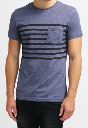 Hombre vistiendo una camiseta azul ajustada con cinco franjas horizontales negras en el pecho y un bolsillo en el lado izquierdo del pecho.