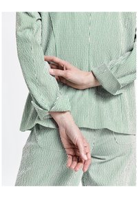 Vêtement en tissu à rayures vertes et blanches, comprenant une veste ajustée avec des manches retroussées et un pantalon assorti, tous deux de texture lisse.