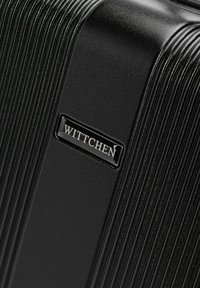 Maleta dura negra con textura lineal y una placa de logo brillante que dice "WITTCHEN". Presenta una forma rectangular y elegante.