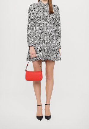 Robe à pois noir et blanc avec manches longues, coupe trapèze ; sac à main rouge avec une anse courte ; escarpins noirs pointus.