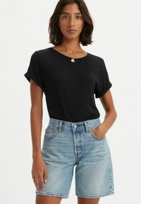 T-shirt noir à manches roulées associé à un short en denim bleu clair taille haute. Design simple avec une coupe décontractée et une texture douce.