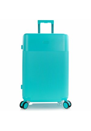 Maleta rígida turquesa con asa telescópica y cuatro ruedas dobles giratorias, mitad inferior texturizada, colocada en posición vertical sobre fondo blanco.