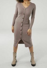 Žebrované šaty s dlouhým rukávem v tlumené mauve barvě, s výstřihem do V a řadou knoflíků vpředu. Délka ke kolenům s bočním rozparkem.