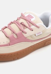 Beżowe zamszowe sneakersy z różowymi skórzanymi akcentami, białą siateczkową podszewką i gumową podeszwą. Posiadają płaskie sznurowadła i naszywkę z logo na języku.