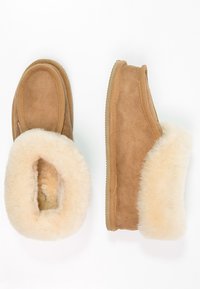 Pantofole in suede tan con morbido rivestimento e bordi in pelliccia sintetica color crema, dotate di punta arrotondata e suola in gomma per una maggiore durata.
