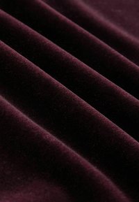 Burgunderroter Samtstoff mit einer weichen, strukturierten Oberfläche, der tiefen Falten aufweist, die seine reiche Farbe und luxuriöse Erscheinung betonen.