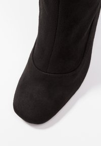 Botín negro de ante hasta el tobillo con punta redonda y superficie lisa. Presenta un diseño sin costuras y un ligero tacón, adecuado para uso formal o informal.