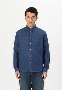 Denim overhemd in donkerblauw met een knoopsluiting kraag, voorzak, lange mouwen en een licht getailleerde pasvorm. Gladde textuur en klassiek ontwerp.