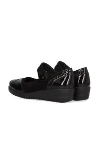 Zapatos tipo Mary Jane negros con una puntera de charol brillante y parte superior de ante suave. Cuenta con una correa de velcro y un tacón bajo tipo cuña.