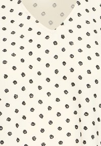 Tissu crème avec un imprimé floral abstrait noir éparpillé et une légère encolure en V visible en haut.