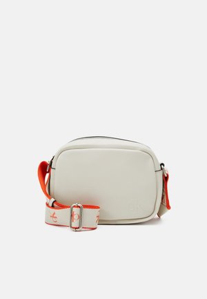 Petit sac bandoulière blanc cassé compact avec une large sangle ajustable beige et orange comportant des logos rouges "ck" et une boucle argentée.