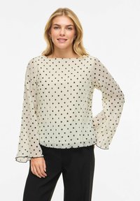 Kremowa bluzka w czarne kropki, z luźnymi długimi rękawami i prostym krojem, z zaokrąglonym dołem i fakturowaną tkaniną.