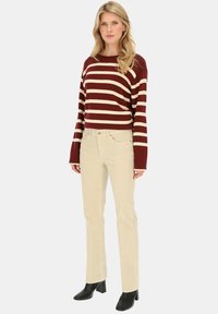 Sweter w paski w kolorze bordowym i kremowym, z szerokimi rękawami, zestawiony z jasnobeżowymi spodniami z kordurowej tkaniny i czarnymi botkami na obcasie. Prosty i casualowy strój.
