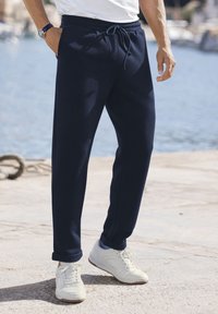 Marineblaue Jogginghose aus weichem Material mit elastischem Bund, Kordelzug, Seitentaschen und umgeschlagenen Säumen, kombiniert mit weißen Sneakers.