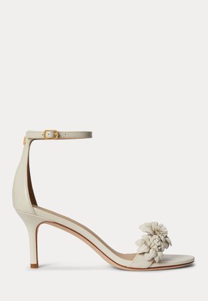 Beige Sandalette mit hohem Absatz, dünnem Knöchelriemen und Schnalle, offener Zehenbereich mit dreidimensionalen Blumenapplikationen verziert.