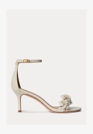Béžová sandála na vysokom podpätku s tenkým remienkom okolo členka a prackou, otvorená špička zdobená trojrozmernými kvetinovými aplikáciami.