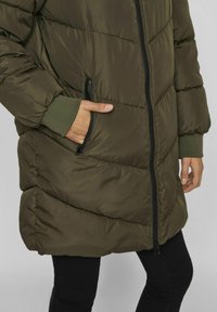 Olivzaļš, garš pūkains mētelis ar rāvējslēdzēja priekšpusi, horizontālām šuvēm, ribotām piedurknēm un sānu kabatām. Gluda auduma un brīvs piegriezums.